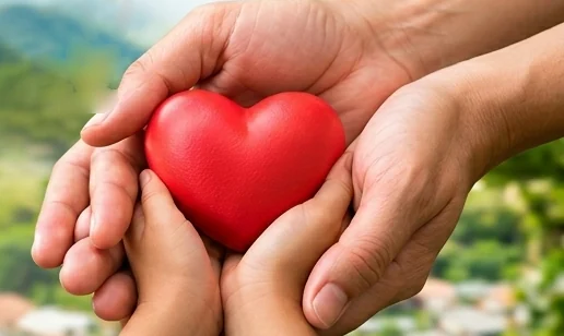 Las manos de un adulto y de un niño sostienen juntas un corazón rojo