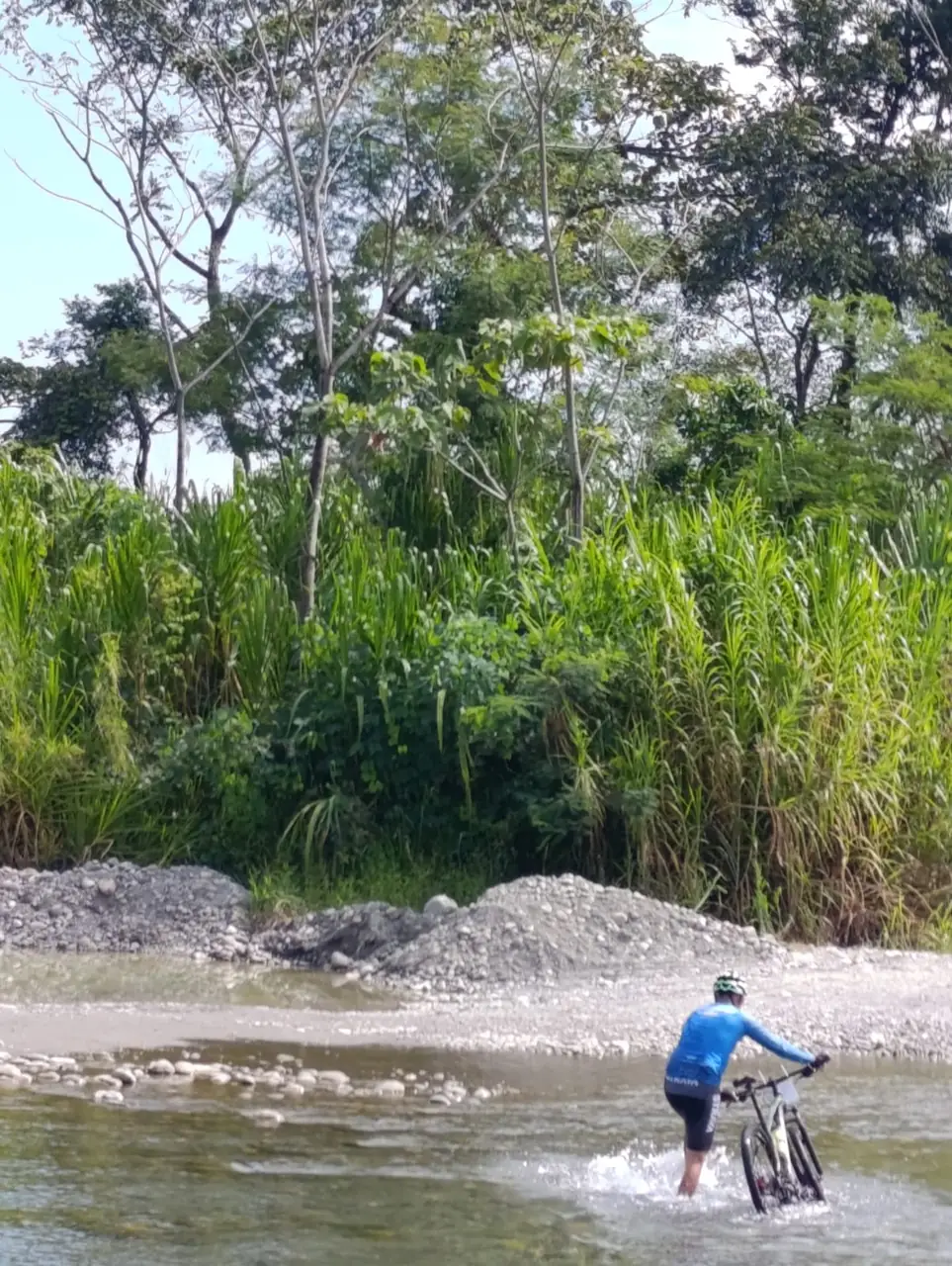 Ciclista con uniforme azul atravesando un río con su bicicleta