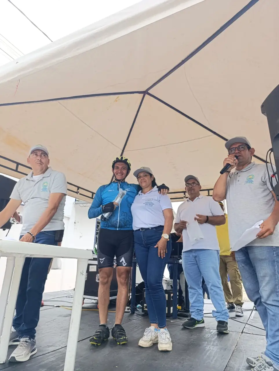 Ciclista de uniforme azul recibe su reconocimiento junto a los organizadores