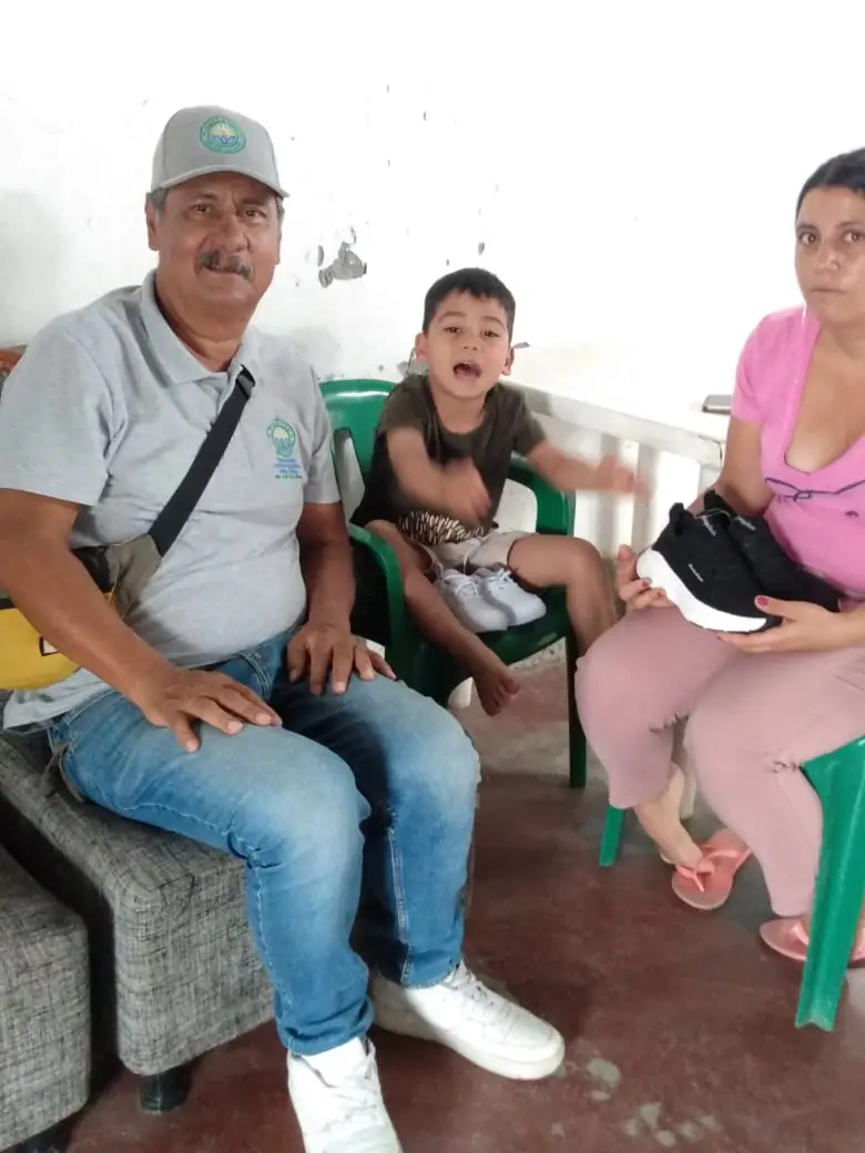 Un integrante de la fundación junto a un niño y su madre, que sostiene los zapatos recibidos