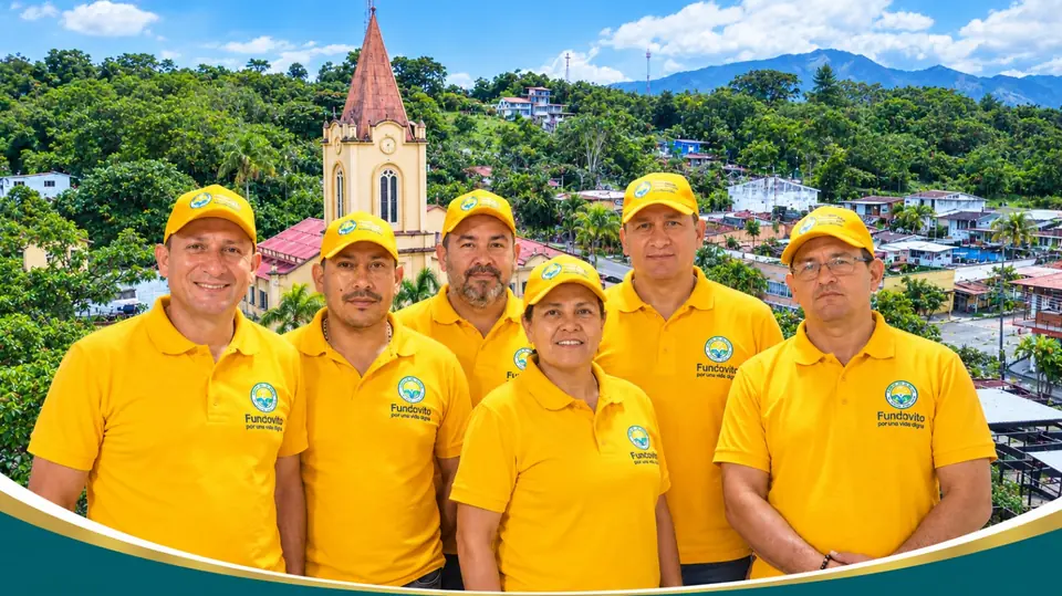 El equipo de la fundación, con camiseta y gorra amarillas, frente a la iglesia y el pueblo, con las montañas al fondo